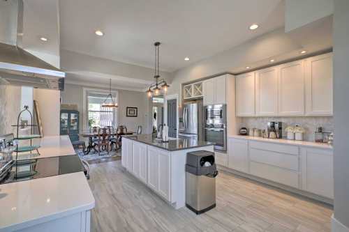 Modern kitchen with white cabinets, stainless steel appliances, and a central island, featuring a dining area in the background.