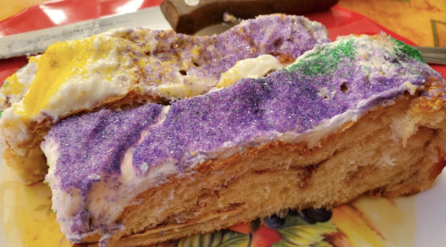 A slice of king cake topped with purple, green, and yellow sugar, resting on a colorful plate.