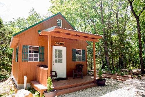 A cozy cabin with a porch, surrounded by trees, featuring a sign that says "CABIN" above the front door.