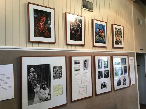 A gallery wall featuring framed photographs, including portraits and still life, displayed in a well-lit room.