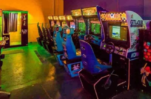 A row of vintage arcade game machines in a dimly lit room with colorful lighting.
