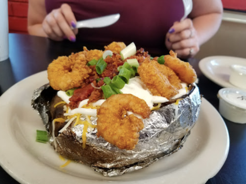 A loaded baked potato topped with shrimp, bacon, green onions, and sour cream, served on a plate.