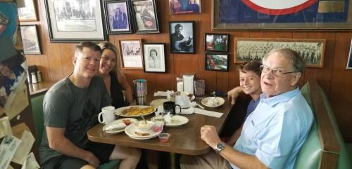 A family enjoys breakfast at a cozy diner, surrounded by framed photos and memorabilia.