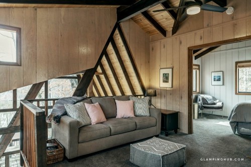 Cozy interior of a cabin with wooden walls, a sofa, and large windows, featuring a warm, inviting atmosphere.
