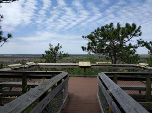 A wooden observation deck with informational signs overlooks a scenic landscape under a partly cloudy sky.