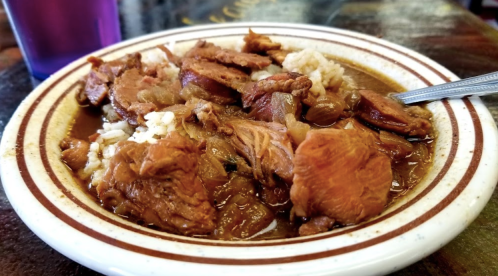 A plate of rice topped with tender, shredded meat in a rich brown sauce, served in a striped bowl.
