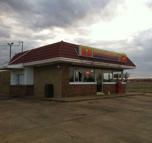 A small fast-food restaurant named "Boomer's" with a red roof and open sign, set against a cloudy sky.