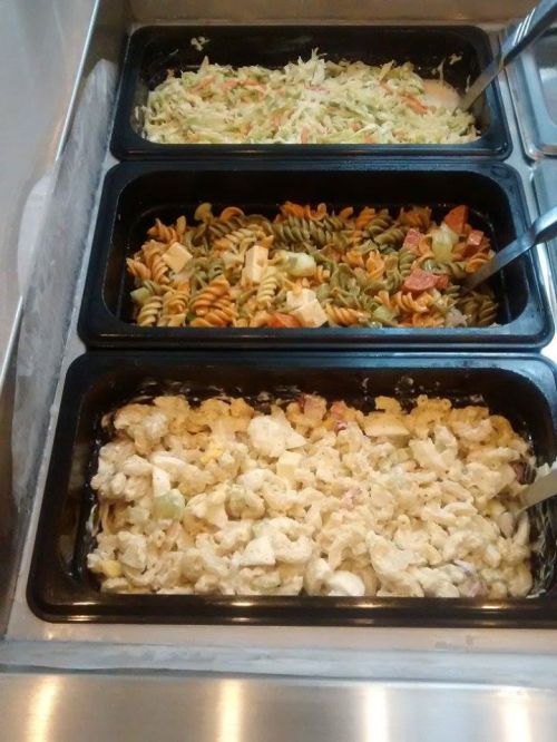Three trays of pasta salads: one with coleslaw, one with rotini and vegetables, and one with creamy macaroni salad.