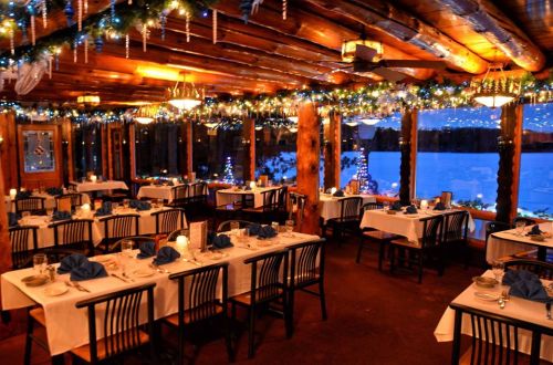 Cozy restaurant interior with festive decorations, tables set for dining, and a view of snowy scenery outside.