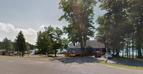 A blue house surrounded by trees near a lake, with parked cars and a gravel driveway.