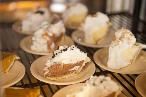 Slices of various cream pies topped with whipped cream on small plates, displayed on a wire rack.