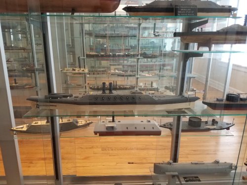 Display of model ships in a glass case, showcasing various designs and sizes in a museum setting.