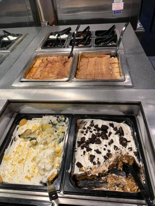 A dessert bar featuring various trays of sweet treats, including cakes and layered desserts, with serving utensils.