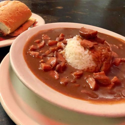 A bowl of rice topped with a rich brown sauce and chunks of meat, served alongside a piece of bread.