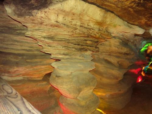 Colorful rock formations with layered textures inside a cave, illuminated by soft, multicolored lights.