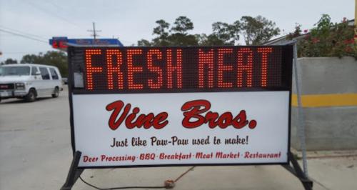 Sign for Vine Bros. advertising "FRESH MEAT" with details about deer processing and a restaurant.