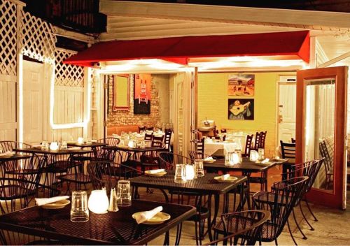 Cozy outdoor restaurant setting with tables, candles, and warm lighting under a red awning.