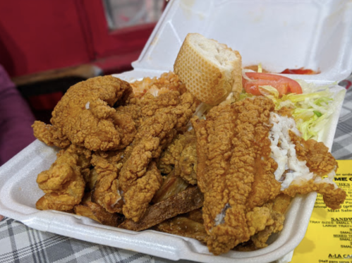A takeout container filled with fried chicken, bread, lettuce, tomatoes, and sides.