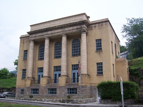 Historic building with tall columns, large windows, and a stone foundation, set against a green hillside.