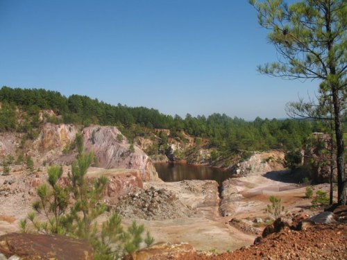 A scenic view of a quarry surrounded by trees and a clear blue sky, with a small body of water in the center.
