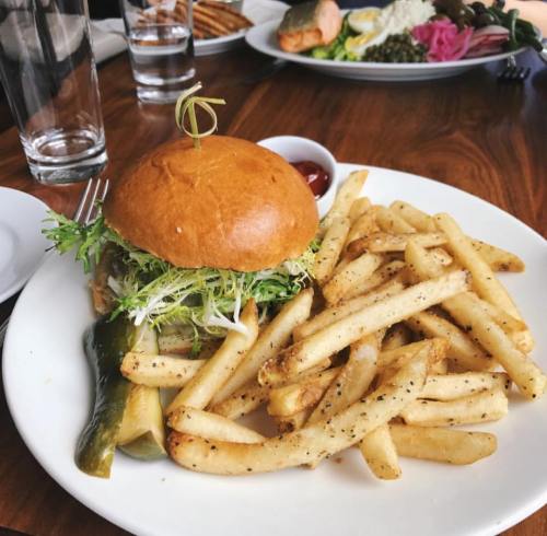 A burger with lettuce on a bun, served with crispy fries and a pickle on a white plate.