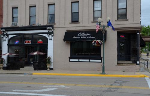 Two adjacent buildings on a street, one with a sign for "Bellissimo" and outdoor seating, the other with a bar entrance.