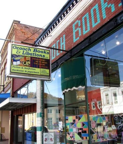 A storefront of Ocooch Books & Libations, featuring colorful window displays and a sign for books and beverages.