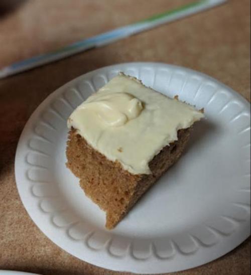A slice of cake on a paper plate, topped with a creamy frosting.