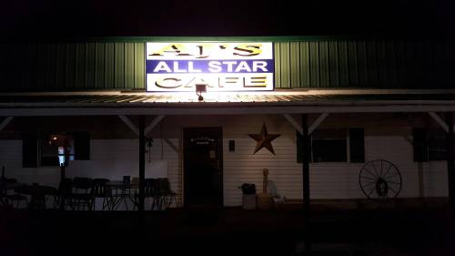 Sign for AJ's All Star Cafe illuminated at night, featuring a star decoration and outdoor seating.