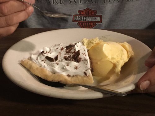 A slice of chocolate cream pie topped with whipped cream and chocolate shavings, served with a scoop of vanilla ice cream.