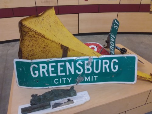 A collection of old street signs and a yellow traffic cone displayed on a table.
