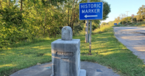 Historic marker for Arkansas, featuring a stone monument beside a road with a directional sign.