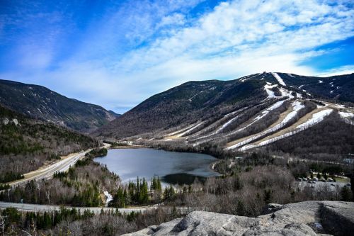 A scenic view of mountains and a lake, with ski slopes visible on the hills under a blue sky.