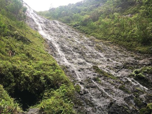 A lush, green hillside with a cascading waterfall flowing down rocky terrain.