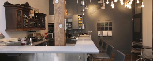 A modern café interior featuring a sleek counter, wooden accents, and stylish lighting with seating in the background.