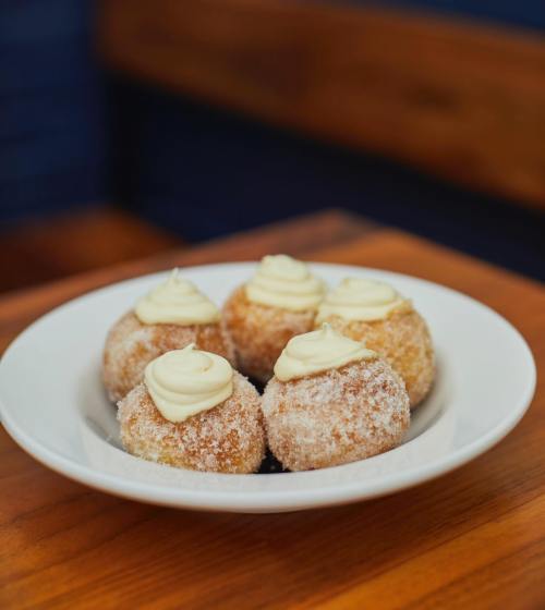 A plate of five sugar-coated doughnut balls topped with creamy frosting, resting on a wooden table.