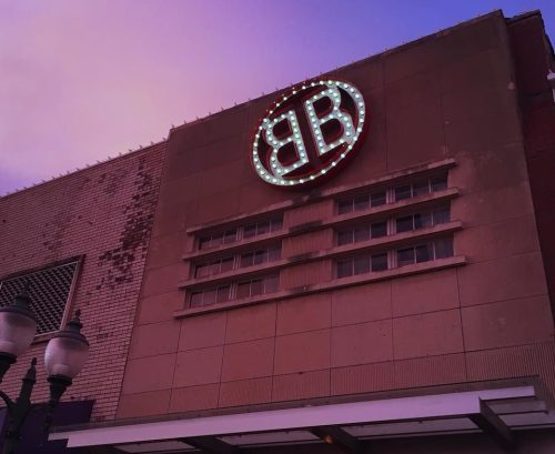 A building facade featuring a large illuminated "BB" sign against a colorful sunset sky.