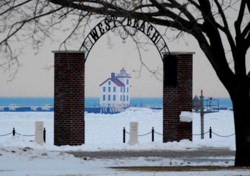 A snowy scene featuring an archway labeled "West Beach" with a lighthouse in the background and a calm lake.