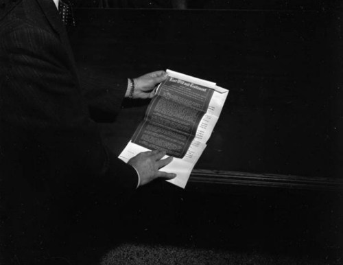 A person holding a document with text, standing near a dark wooden table.