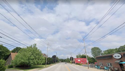 A street view with power lines, trees, and buildings under a cloudy sky.