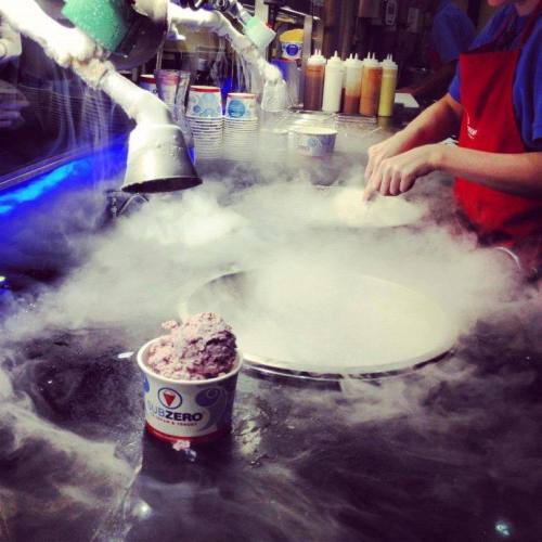 A dessert shop with a worker preparing ice cream using liquid nitrogen, creating a misty effect around the counter.