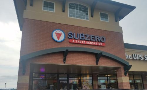 Sign for SubZero, an ice cream shop, featuring a logo and the tagline "A Taste Sensation" on a brick building.