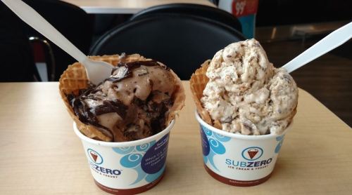 Two waffle bowls filled with ice cream: one with chocolate and fudge, the other with cookies and cream.