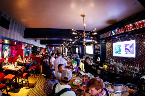 A lively bar scene with patrons socializing, colorful decor, and a well-stocked bar in a vibrant atmosphere.