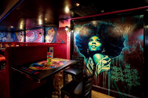 A vibrant restaurant interior featuring colorful murals, including a striking portrait of a woman with an afro.