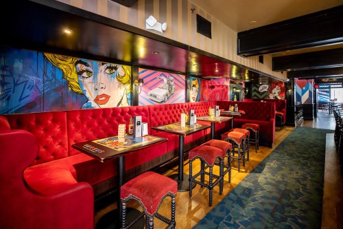 Vibrant restaurant interior featuring red booths, artistic wall murals, and stylish tables.