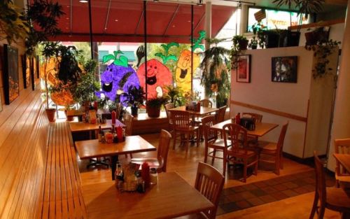 Cozy restaurant interior with wooden tables, plants, and colorful fruit-themed window art.