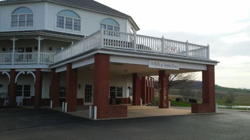 A large building with a covered entrance, featuring a sign that reads "The Inn at Amish Door" and a scenic background.