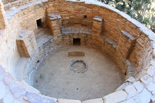 Circular stone structure with walls and small openings, featuring a central stone circle and sandy floor.