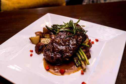 A gourmet plate featuring a steak with asparagus, roasted potatoes, and a rich sauce, garnished with herbs.